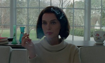 Movie still from “Jackie” (2016), directed by Pablo Larraín – A woman smoking a cigarette while sitting in front of a window; Close Up shot, Over the shoulder angle