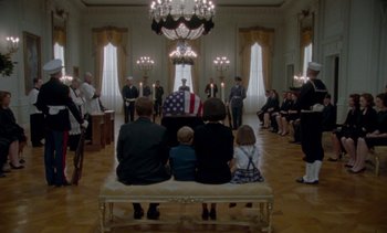 Movie still from “Jackie” (2016), directed by Pablo Larraín – A group of people sitting on a bench in a room; Wide shot, Low angle