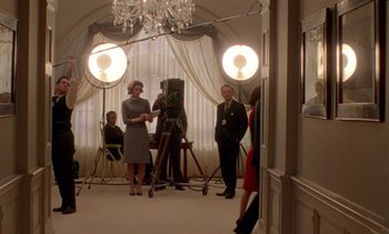 Movie still from “Jackie” (2016), directed by Pablo Larraín – A woman in a gray dress standing next to a man in a suit; Wide shot, Low angle