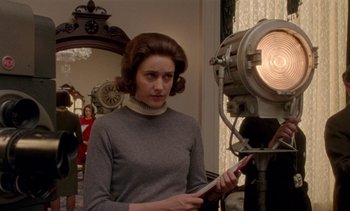 Movie still from “Jackie” (2016), directed by Pablo Larraín – A woman standing in front of a camera holding a paper; Medium shot, Over the shoulder angle