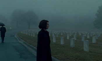 Movie still from “Jackie” (2016), directed by Pablo Larraín – A person standing in front of a field of grave markers; Wide shot, Over the shoulder angle