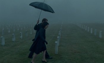 Movie still from “Jackie” (2016), directed by Pablo Larraín – A man and a woman walking through a cemetery holding an umbrella; Wide shot, High angle