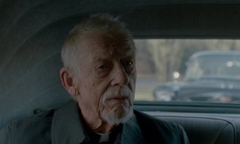 Movie still from “Jackie” (2016), directed by Pablo Larraín – An older man sitting in a car looking out the window; Close Up shot, Over the shoulder angle