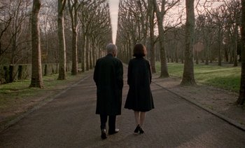 Movie still from “Jackie” (2016), directed by Pablo Larraín – A man and a woman walking down a path in the woods; Wide shot, Over the shoulder angle