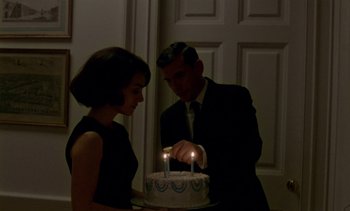 Movie still from “Jackie” (2016), directed by Pablo Larraín – A man and a woman lighting candles on top of a birthday cake; Medium shot, High angle