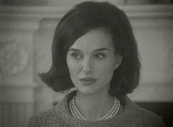 Movie still from “Jackie” (2016), directed by Pablo Larraín – An old photo of a woman wearing a sweater and pearl necklace; Close Up shot, Over the shoulder angle