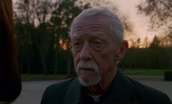 Movie still from “Jackie” (2016), directed by Pablo Larraín – An older man wearing a priest's collar; Close Up shot, Low angle