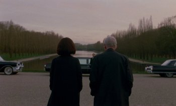 Movie still from “Jackie” (2016), directed by Pablo Larraín – A man and a woman standing in front of a car; Wide shot, Over the shoulder angle