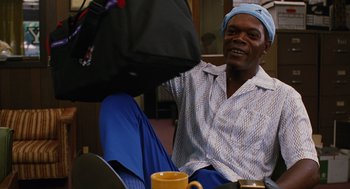Movie still from “Jackie Brown” (1997), directed by Quentin Tarantino – A man sitting on a chair with a bag in front of him; Medium shot, Low angle