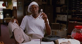 Movie still from “Jackie Brown” (1997), directed by Quentin Tarantino – A man sitting at a table holding up a bottle of water; Medium shot, High angle