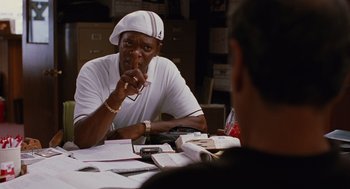 Movie still from “Jackie Brown” (1997), directed by Quentin Tarantino – A man sitting at a table in front of papers; Medium shot, Over the shoulder angle