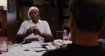 Movie still from “Jackie Brown” (1997), directed by Quentin Tarantino – A man sitting at a table with a stack of money; Medium shot, Over the shoulder angle