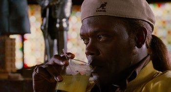 Movie still from “Jackie Brown” (1997), directed by Quentin Tarantino – A man drinking a glass of orange juice with a straw; Close Up shot, Over the shoulder angle