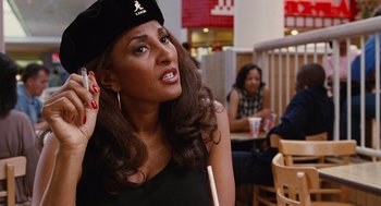 Movie still from “Jackie Brown” (1997), directed by Quentin Tarantino – A woman in a black dress and a black hat is holding her hand up to her face; Close Up shot, Over the shoulder angle