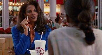 Movie still from “Jackie Brown” (1997), directed by Quentin Tarantino – A woman sitting at a table with a drink in front of her face; Medium shot, Over the shoulder angle