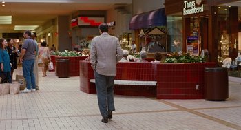Movie still from “Jackie Brown” (1997), directed by Quentin Tarantino – A man walking down a sidewalk in a shopping center; Wide shot, Over the shoulder angle