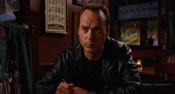 Movie still from “Jackie Brown” (1997), directed by Quentin Tarantino – A man in a black leather jacket sitting in front of a wall; Close Up shot, Over the shoulder angle