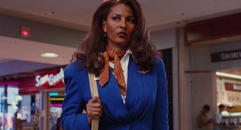 Movie still from “Jackie Brown” (1997), directed by Quentin Tarantino – A woman in a blue suit and orange tie holding a bag; Medium shot, Low angle