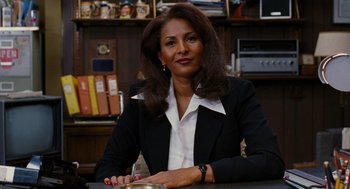 Movie still from “Jackie Brown” (1997), directed by Quentin Tarantino – A woman sitting at a table in front of a book case; Medium shot, Low angle