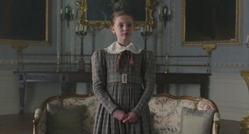 Movie still from “Jane Eyre” (2011), directed by Cary Joji Fukunaga – A girl in a dress standing in front of a couch; Medium shot, Low angle
