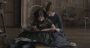 Movie still from “Jane Eyre” (2011), directed by Cary Joji Fukunaga – A woman and a girl sitting on the floor looking at a book; Medium shot, High angle
