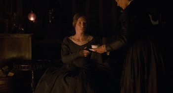 Movie still from “Jane Eyre” (2011), directed by Cary Joji Fukunaga – A woman in a black dress is holding a cup; Medium shot, High angle