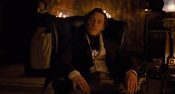Movie still from “Jane Eyre” (2011), directed by Cary Joji Fukunaga – A man sitting in a chair in front of a painting; Medium shot, High angle