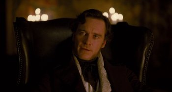 Movie still from “Jane Eyre” (2011), directed by Cary Joji Fukunaga – A person sitting in a chair wearing a suit; Close Up shot, Over the shoulder angle