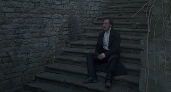 Movie still from “Jane Eyre” (2011), directed by Cary Joji Fukunaga – A man sitting on some steps wearing a suit; Wide shot, High angle