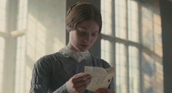 Movie still from “Jane Eyre” (2011), directed by Cary Joji Fukunaga – A young woman holding a piece of paper in front of a window; Close Up shot, Low angle