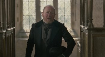 Movie still from “Jane Eyre” (2011), directed by Cary Joji Fukunaga – An older man in a suit and a hat in front of stained glass windows; Medium shot, Low angle
