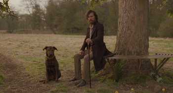 Movie still from “Jane Eyre” (2011), directed by Cary Joji Fukunaga – A man sitting on a bench next to a brown dog; Wide shot, Low angle