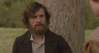Movie still from “Jane Eyre” (2011), directed by Cary Joji Fukunaga – A man with long hair and a beard is sitting in front of a tree; Close Up shot, Over the shoulder angle