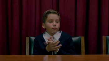 Movie still from “El Jeremías” (2015), directed by Anwar Safa – A boy sitting at a table with his hands clasped together; Medium shot, High angle