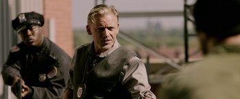 Movie still from “Jigsaw” (2017), directed by Michael Spierig – A man in a vest and tie standing in front of a building; Close Up shot, Over the shoulder angle