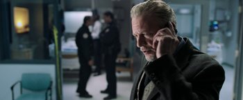 Movie still from “Jigsaw” (2017), directed by Michael Spierig – An older man talking on a cell phone in front of a group of people; Close Up shot, Low angle