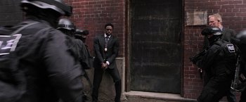 Movie still from “Jigsaw” (2017), directed by Michael Spierig – A man leaning against a brick wall in front of a building; Wide shot, Over the shoulder angle