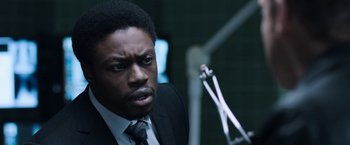 Movie still from “Jigsaw” (2017), directed by Michael Spierig – A man wearing a suit and tie in front of a microphone; Close Up shot, Over the shoulder angle