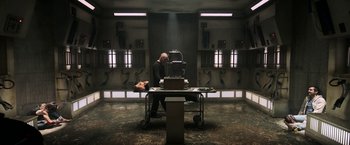Movie still from “Jigsaw” (2017), directed by Michael Spierig – A man sitting at a table in front of an electric device; Wide shot, High angle
