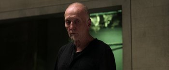 Movie still from “Jigsaw” (2017), directed by Michael Spierig – An older man in a black shirt is looking at the camera; Close Up shot, Low angle