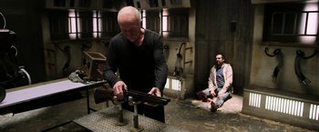 Movie still from “Jigsaw” (2017), directed by Michael Spierig – A man in black shirt holding a gun in a room with other men; Medium shot, High angle