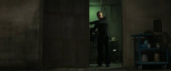 Movie still from “Jigsaw” (2017), directed by Michael Spierig – A man standing next to a wall in a dark room; Wide shot, Low angle