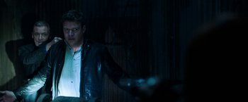 Movie still from “Jigsaw” (2017), directed by Michael Spierig – A man wearing a leather jacket standing in a dark room; Medium shot, Over the shoulder angle