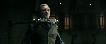 Movie still from “Jigsaw” (2017), directed by Michael Spierig – A man in a vest and tie holding a device in his mouth; Medium shot, Low angle