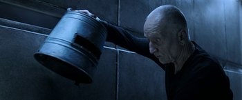 Movie still from “Jigsaw” (2017), directed by Michael Spierig – An older man holding a bucket in a dark room; Close Up shot, Low angle