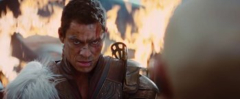 Movie still from “John Carter” (2012), directed by Andrew Stanton – A person holding a sword with fire in the background; Close Up shot, Over the shoulder angle
