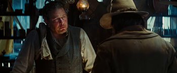 Movie still from “John Carter” (2012), directed by Andrew Stanton – A man standing next to another man wearing a hat; Medium shot, Over the shoulder angle