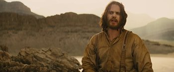 Movie still from “John Carter” (2012), directed by Andrew Stanton – A man with long brown hair standing in front of a mountain; Medium shot, Over the shoulder angle
