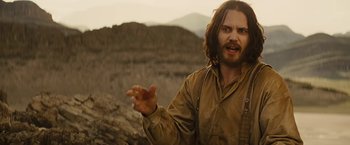 Movie still from “John Carter” (2012), directed by Andrew Stanton – A man standing on top of a mountain with his hands outstretched; Medium shot, Over the shoulder angle