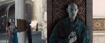 Movie still from “John Carter” (2012), directed by Andrew Stanton – A bald man in a black robe holding a silver object; Medium shot, Over the shoulder angle